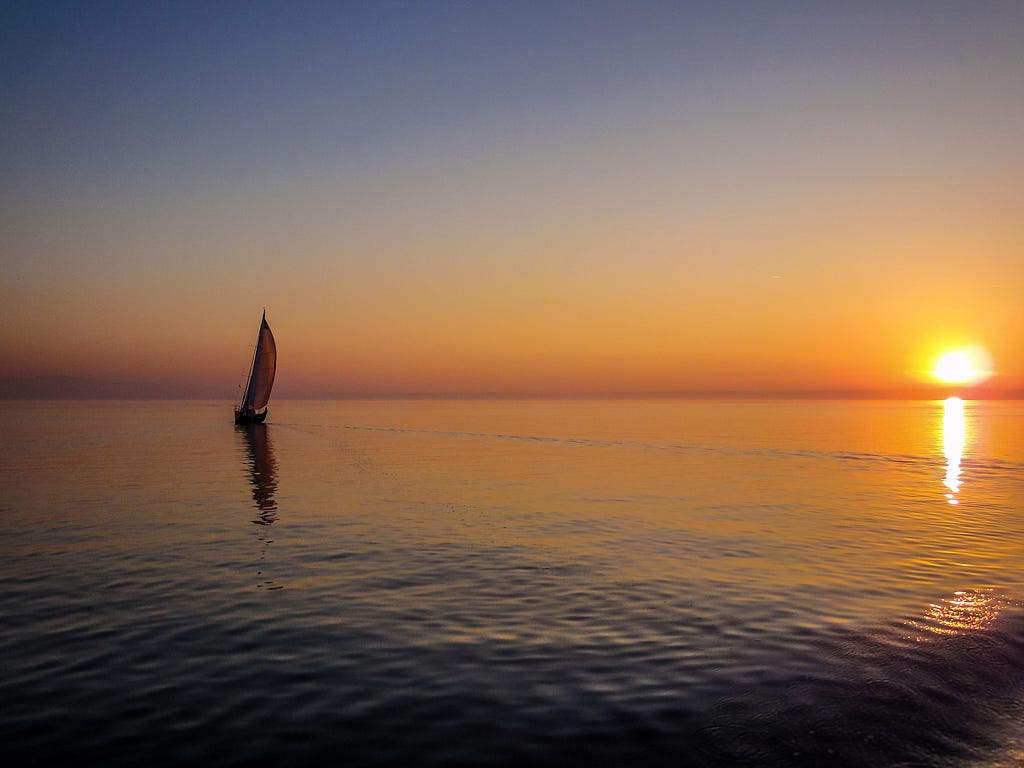 Barco velejando em alto mar em sentido ao por do sol