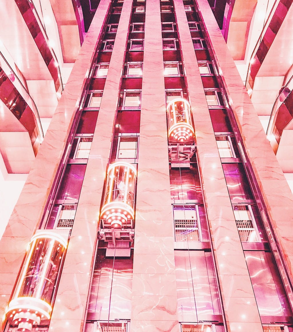 A pink facade with three bright elevators going upwards.