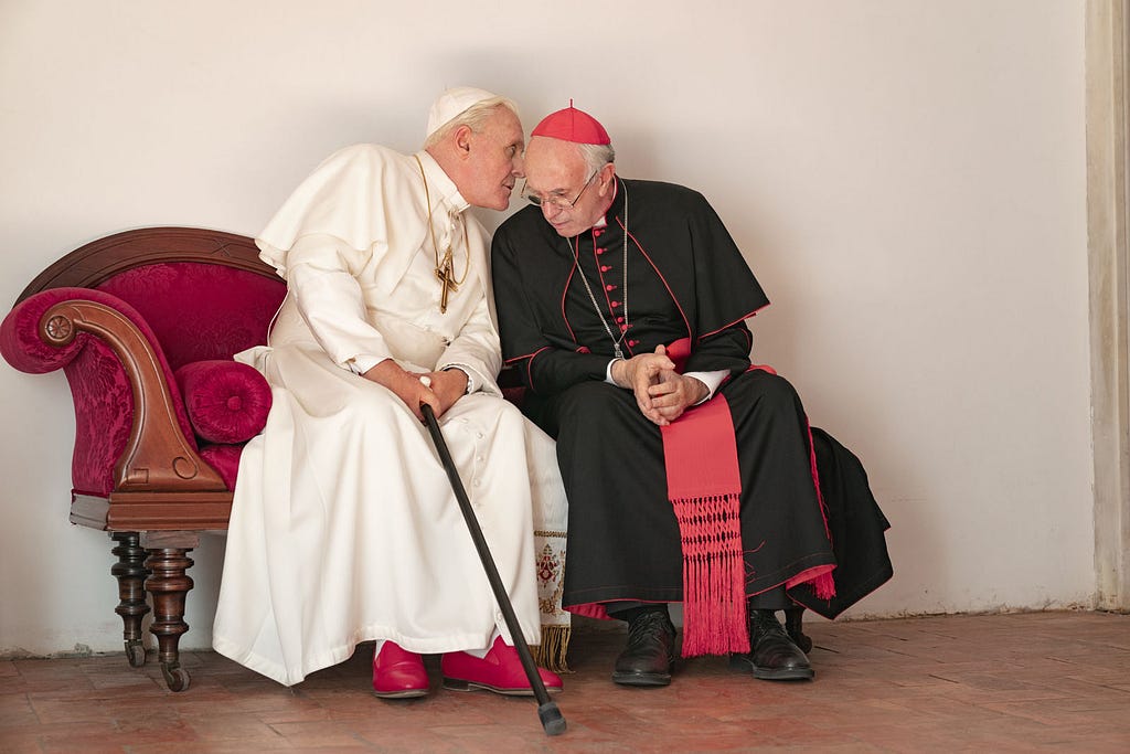 A scene from the Two Popes: Pope Benedict leans to Cardinal Bergoglio’s ear