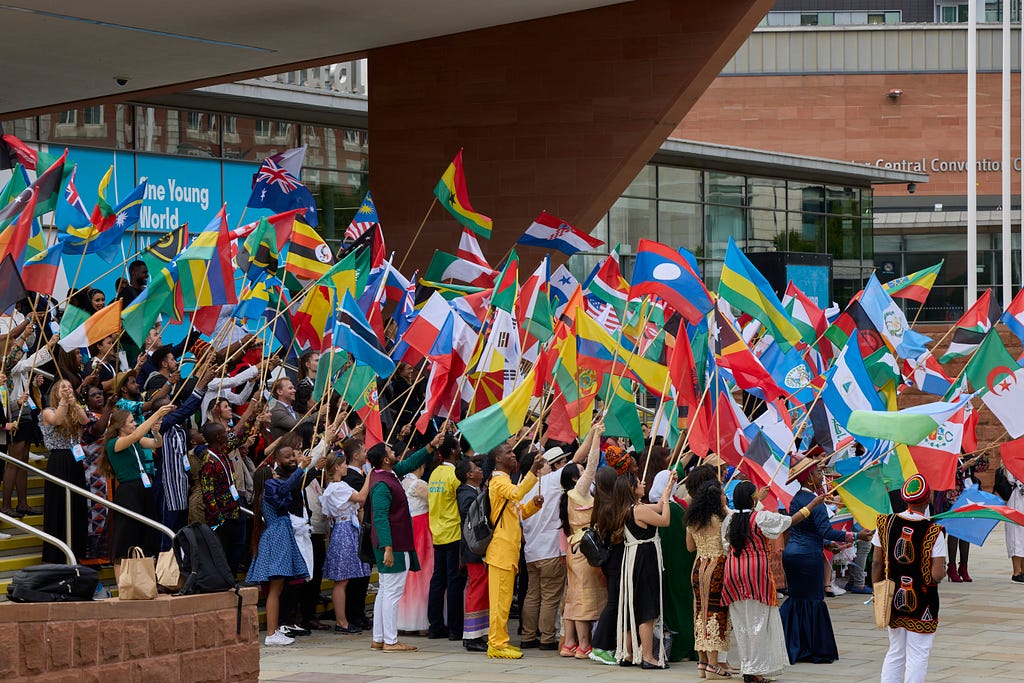 A large group of young leaders stand in a group waving flags from countries around the world.