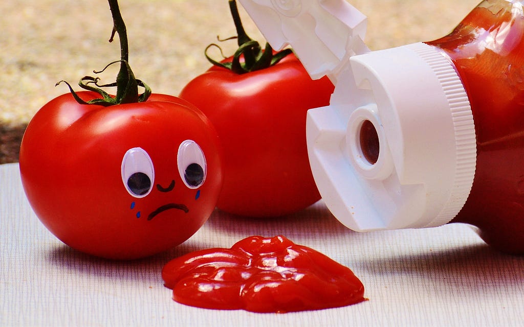 Tomato with a sad face in front of poured ketchup sauce