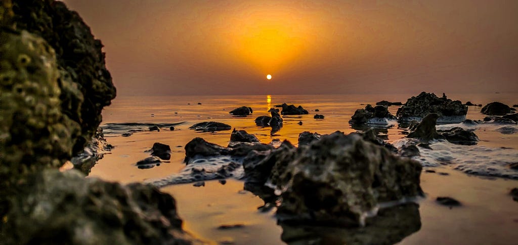 A sun sets over a lake filled with rocks.