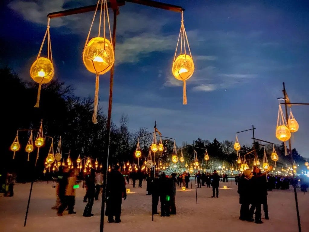 A group of visitors walk through a candlelit area in Minneaoplis. Candles hang from ropes attached to poles.