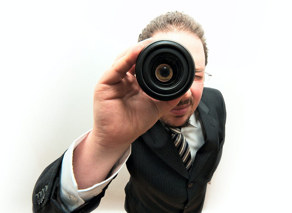 a person wearing a suit and glasses holding a spyglass over one eye