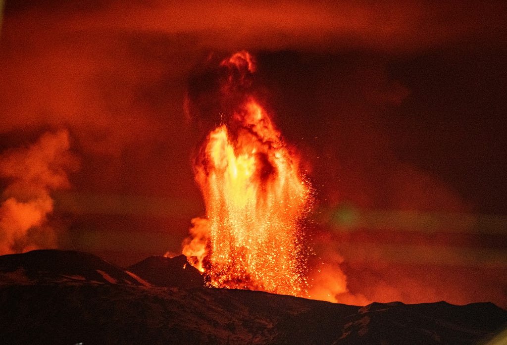 A fountain of orange-red lava shooting into the air during the nighttime.