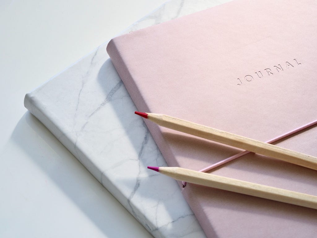 An elegant, pink and light gray color journals on a table with pencils.