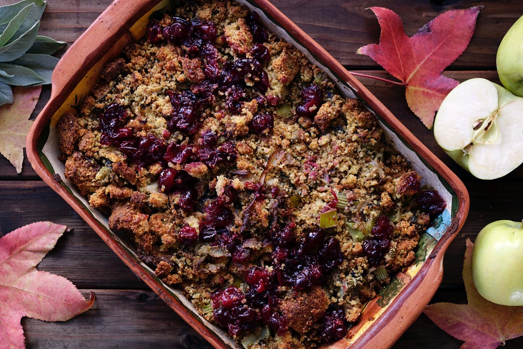 Cranberry stuffing in a baking dish on a wooden table. Fall leaves and apples are displayed next to the dish.