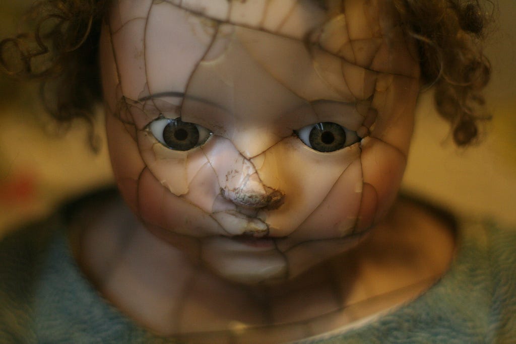 Porcelan doll face that is cracked and looking down and with the closed mouth, looking scared.