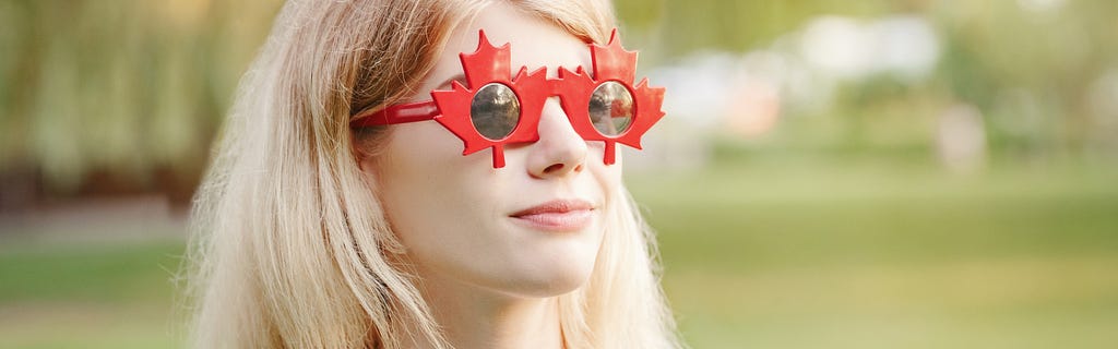 A blonde Canadian woman wearing maple leaf sunglasses