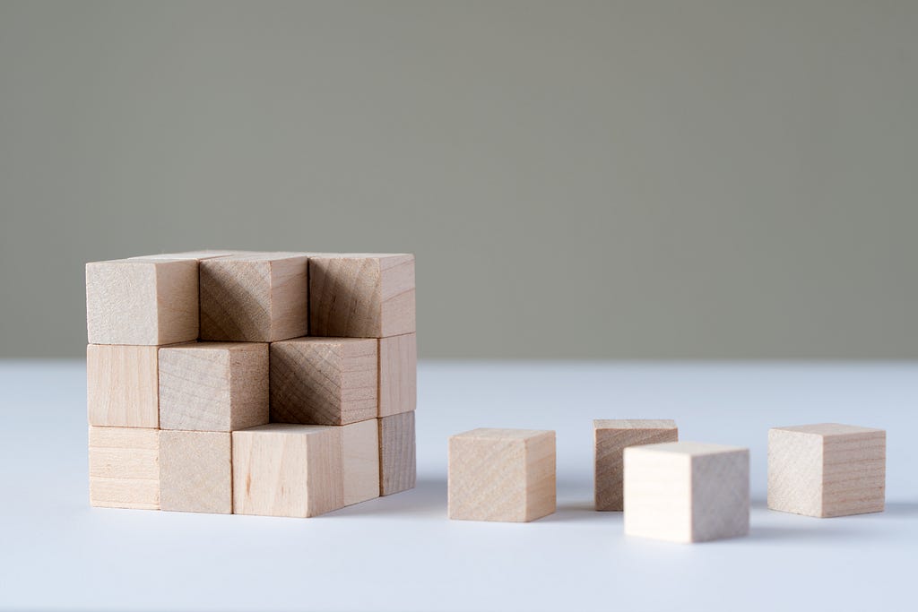 An image of wooden blocks stacked, almost forming a cube, but four of the individual blocks are removed from the cube and sitting next to it.
