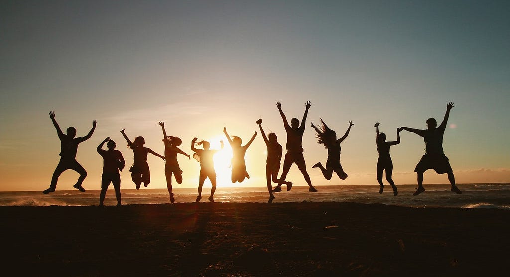 An image of a group of people jumping in the air with setting sun behind them.