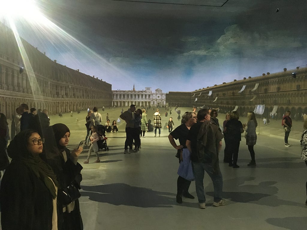 Two pieces by Canaletto of Piazza San Marco are combined and projected onto all sides of a large room to create the impression of being in the square. Lots of (real!) tourists mill around
