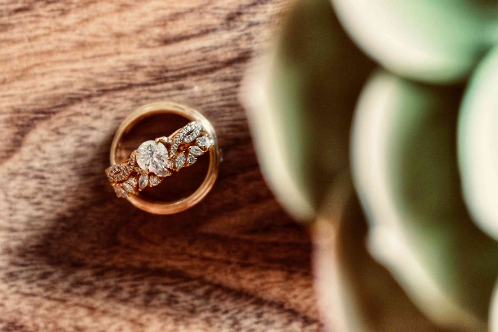 A wedding band and engagement ring together on display on a wooden table.