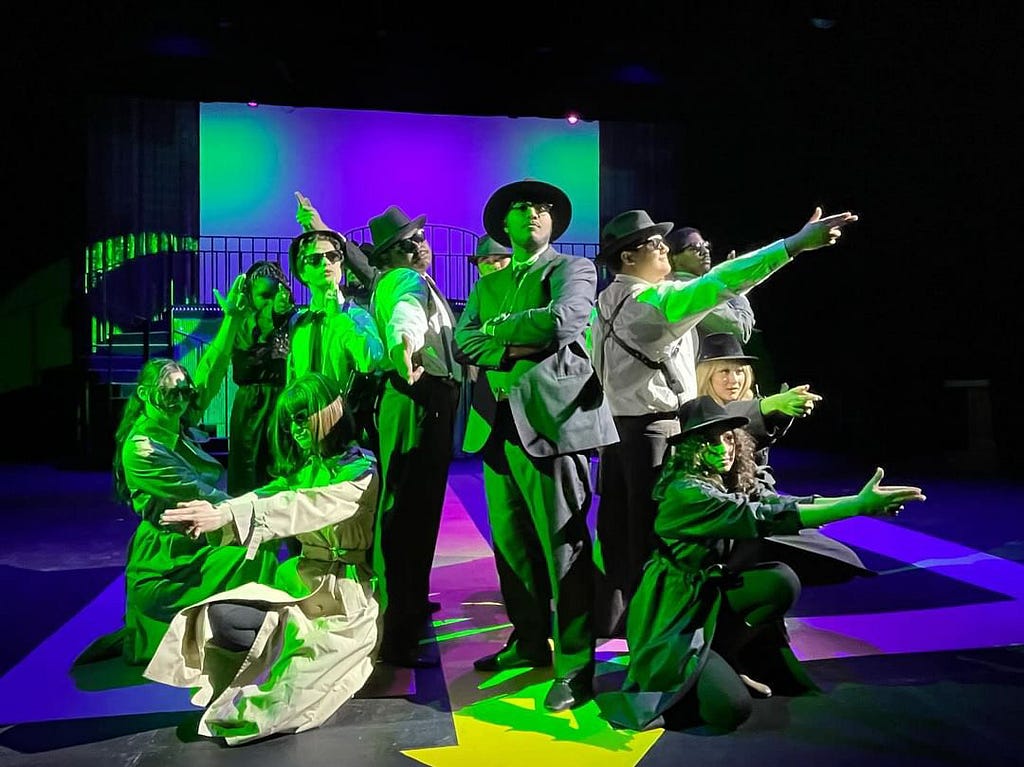 Photo of the ensamble and Hanratty during a number, bathed in green light.