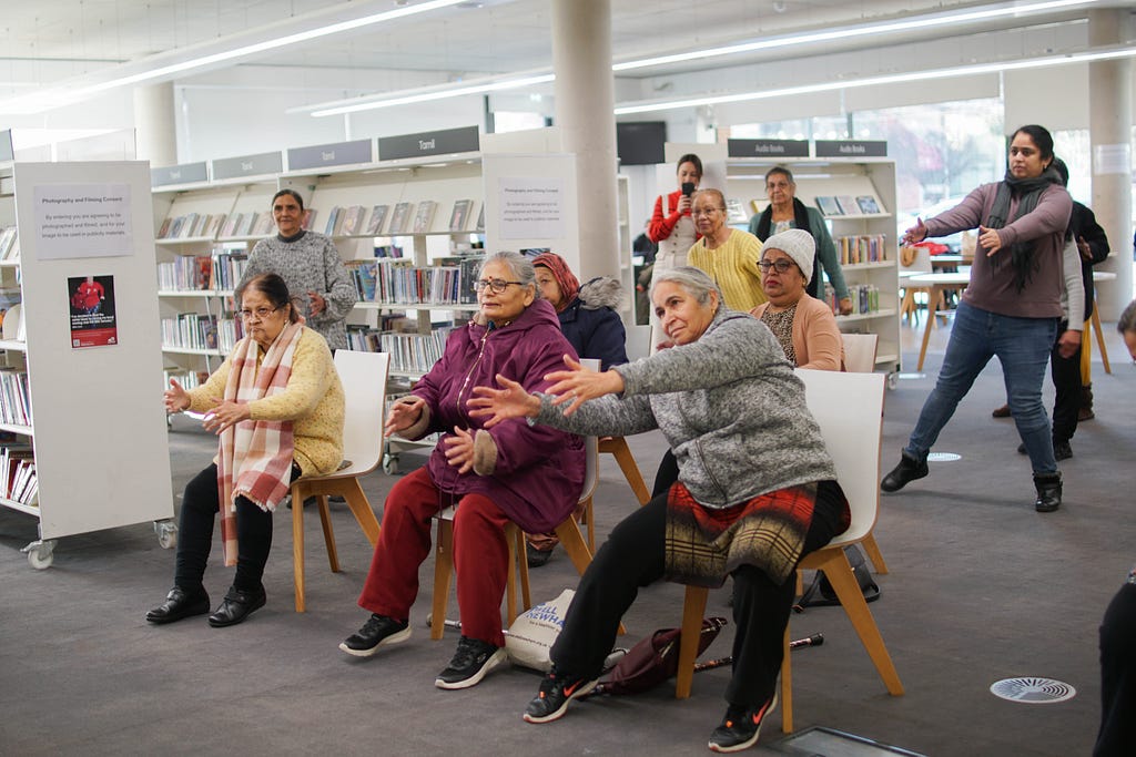 An image of about ten guests, predominantly South Asian heritage but of all ages, stretching together in a library.