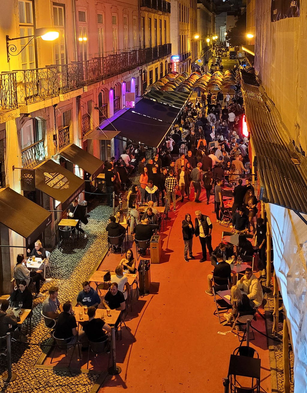 Imagem da rua rosa, local onde acontecem os happy hours do evento, a rua tem a cor rosa no chão, vários bares e restaurantes e muitas pessoas caminhado nela