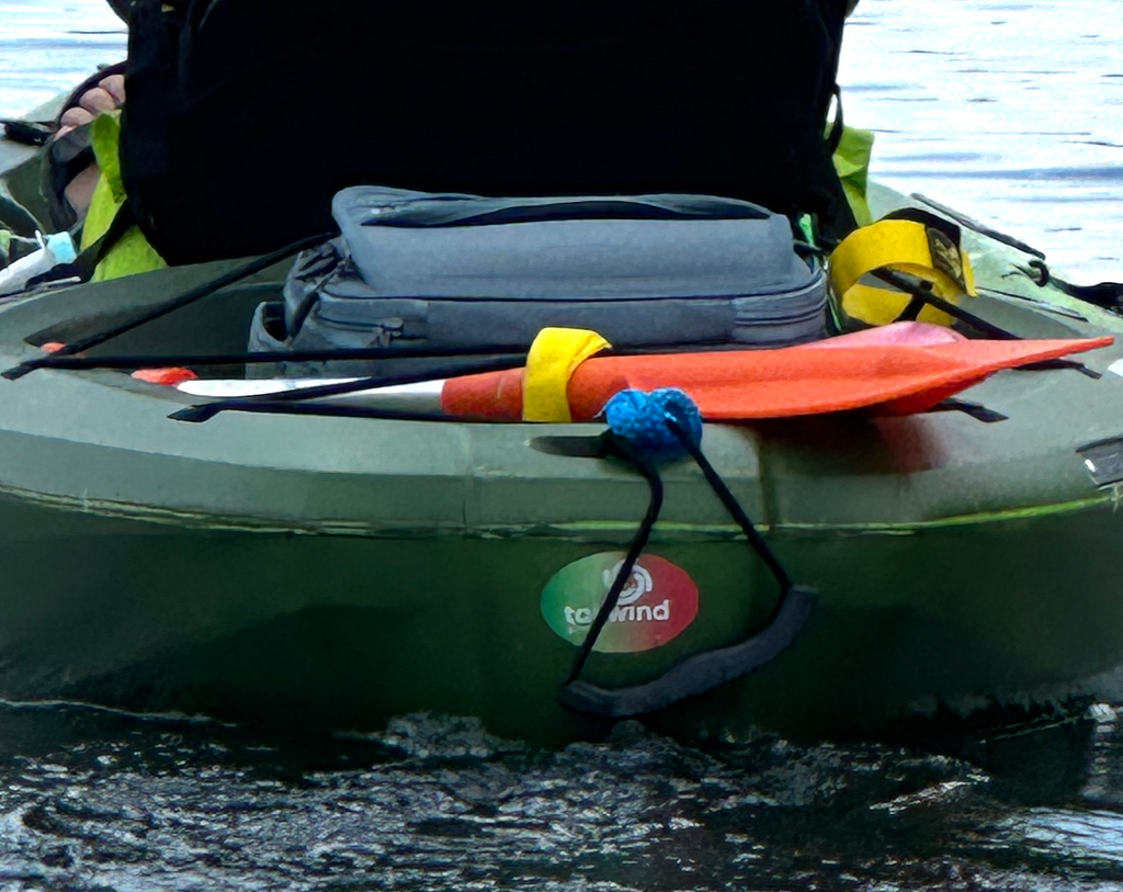 Back of a green kayak in water with a green and red Tailwind sticker.