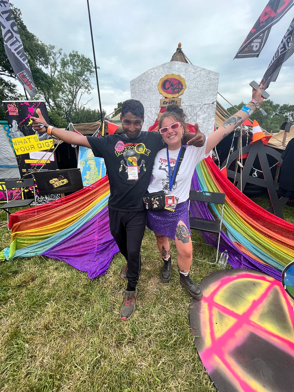 Two Gig Buddies embracing with their arms in the air outside a colourful tent