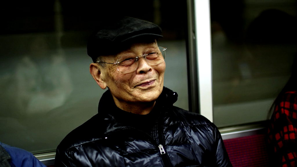 An old man, Jiro, sits smiling on a subway train