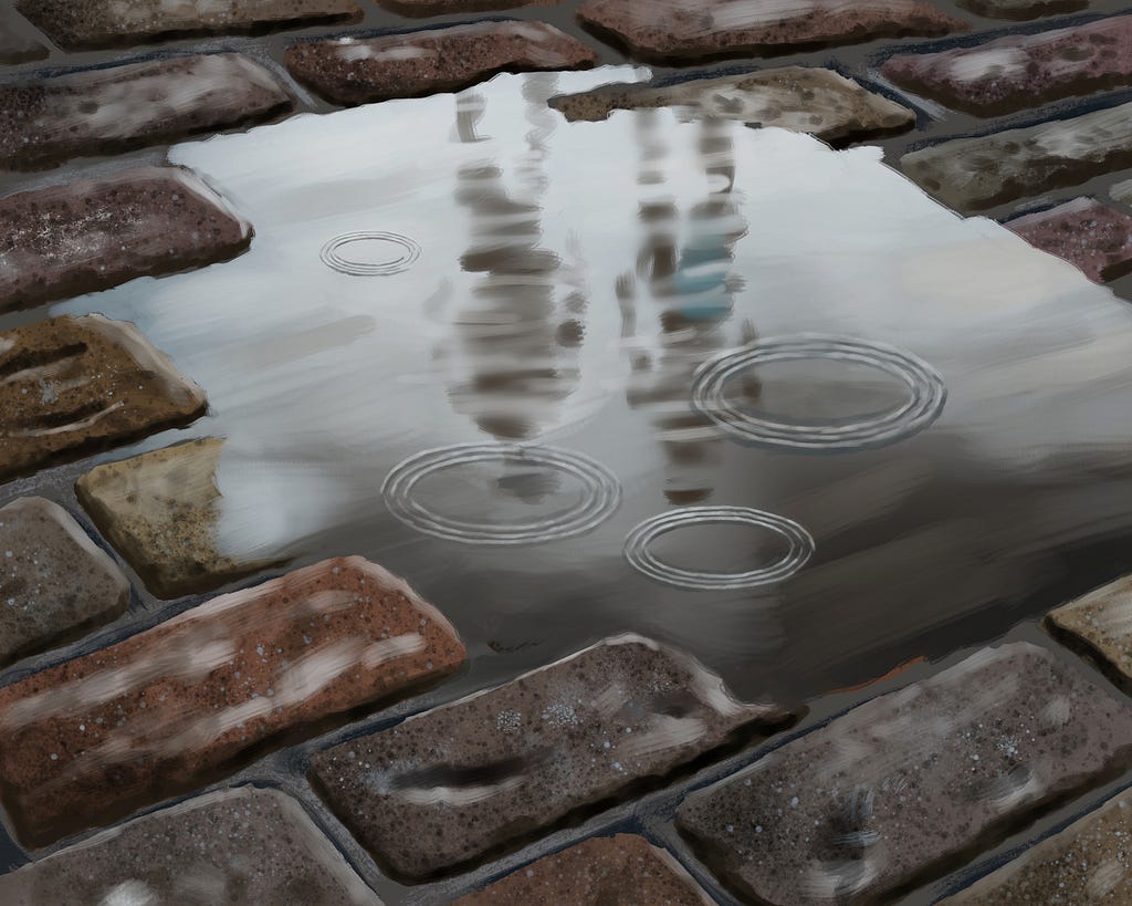 A puddle has formed in a sunken area of a cobblestone road after a rain. A few raindrops hit the puddle and create ripples.