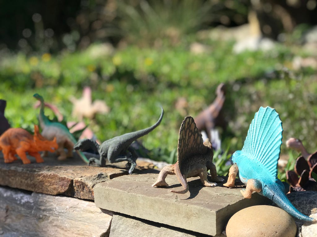 Colorful toy dinosaurs on stone fence with grass in background.