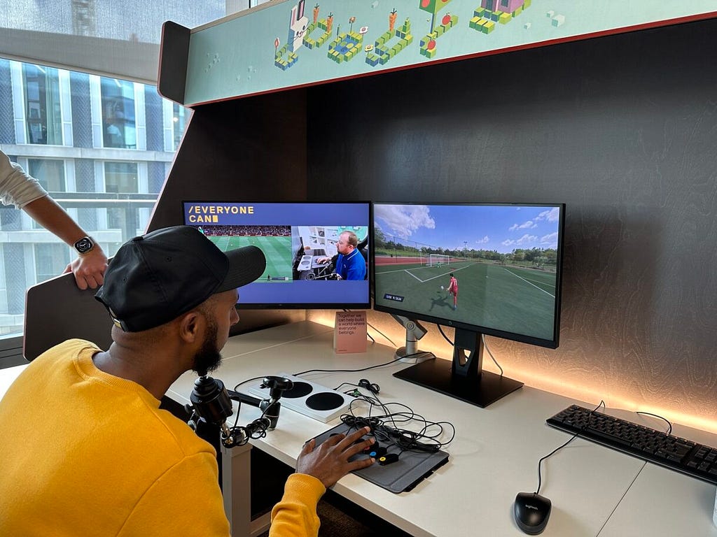 Alieid sits in front of a screen playing Fifa using his chin to navigate and drive momentum of the player forward and buttons to do actions like shoot for goal.