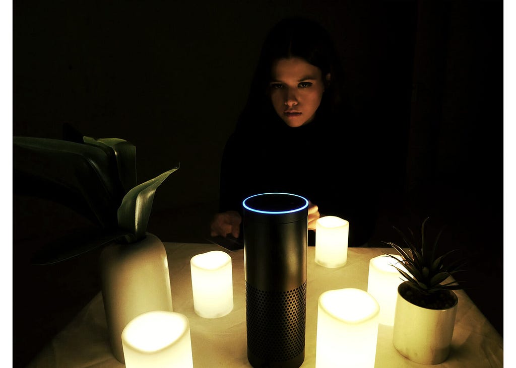 The author sits in the dark behind the Amazon Echo, which is surrounded by lit candles in a seance-style set up.