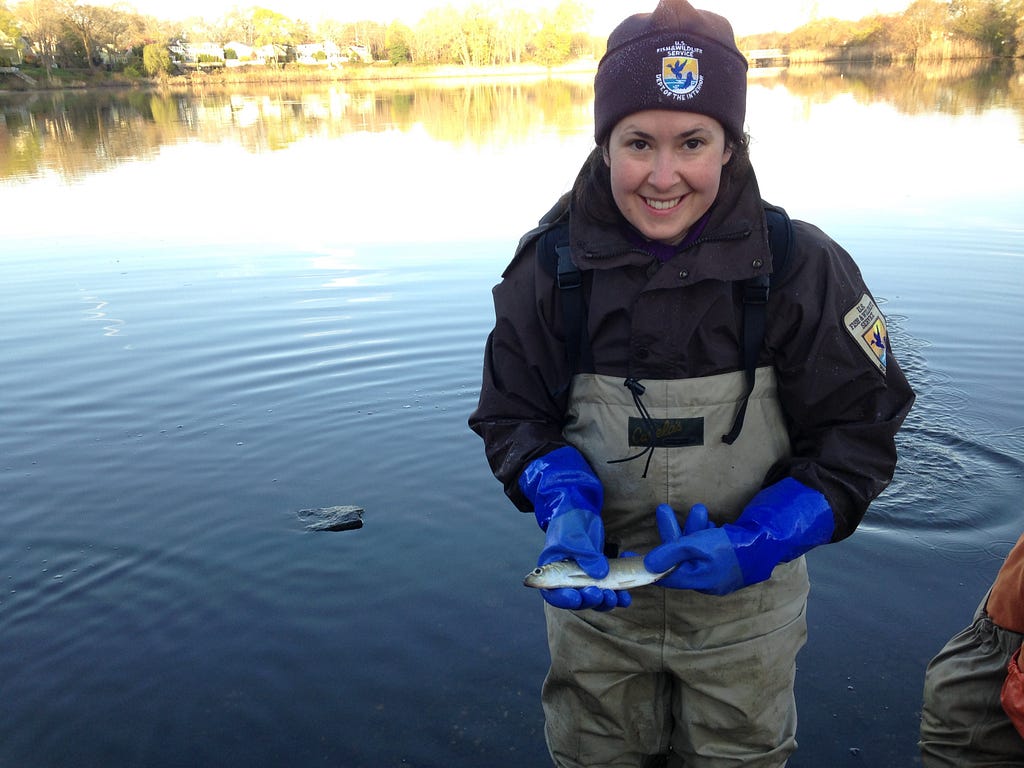 a woman in waders smiles and holds a fish
