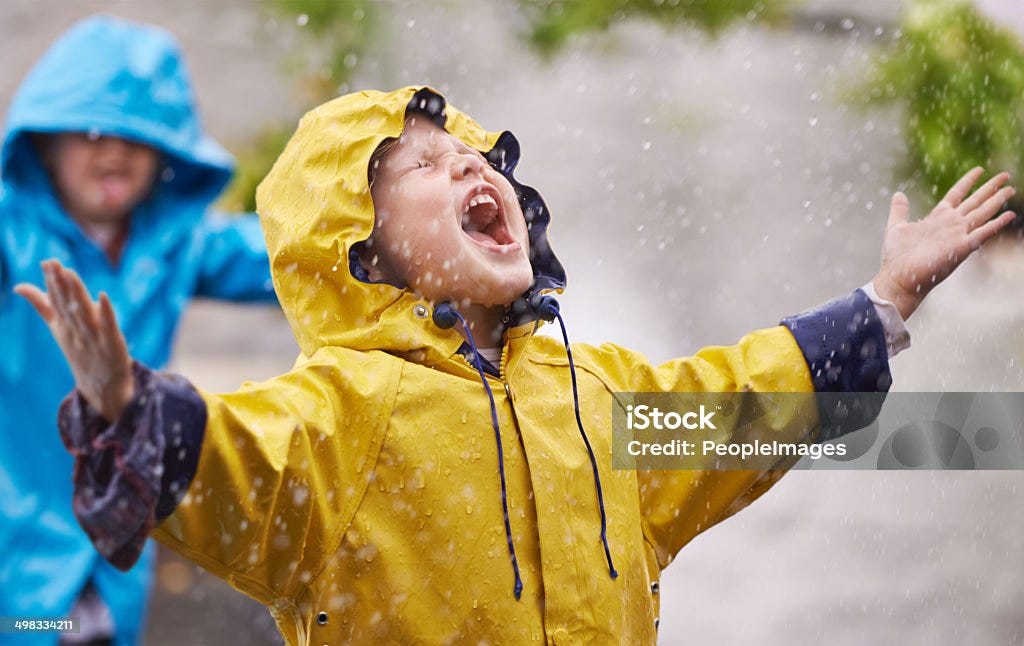 Uma criança sendo bem feliz na chuva, de braços abertos para a felicidade ❤