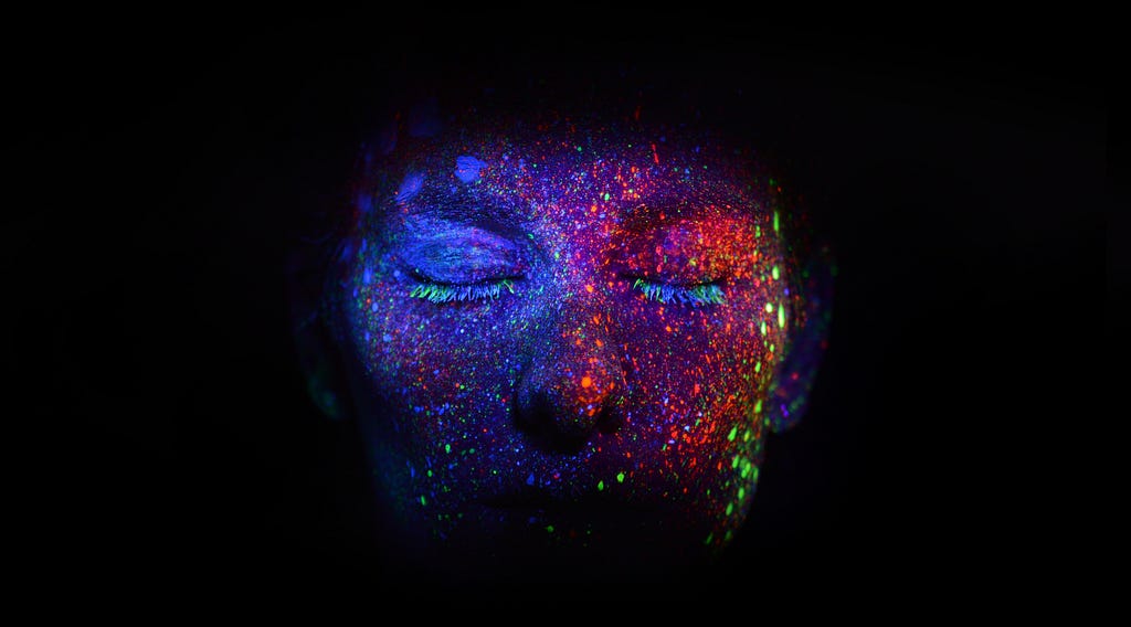 An image of a person’s face covered in glow in the dark paint splatters.