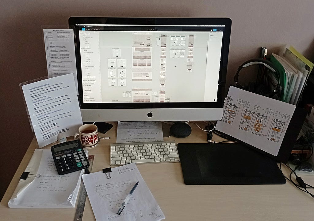 Photo of my working desktop with my computer, notes, sketches, papers, cup etc.