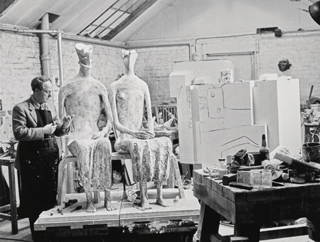 A sculptor Henry Moore at his studio next to his two large human shaped sculptures.