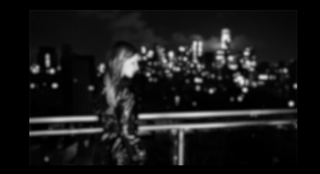 A blurred image of a woman standing outside on a balcony at nighttime