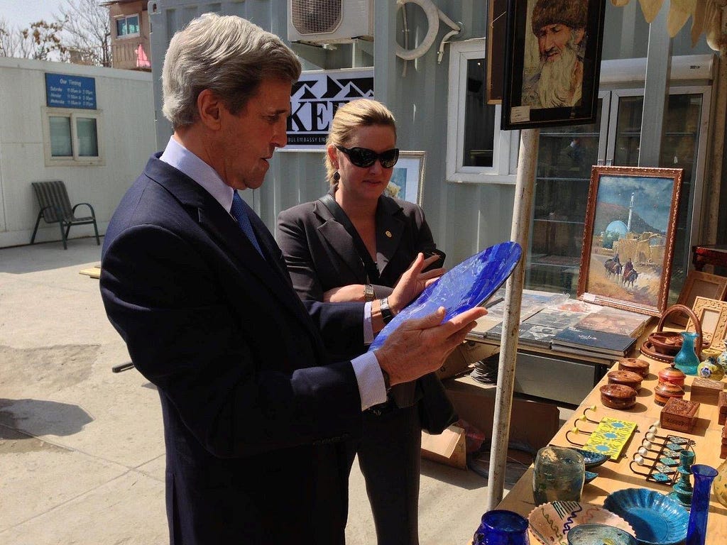 Jennifer Davis and former Sec. of State John Kerry inspect a piece of pottery at an outdoor market