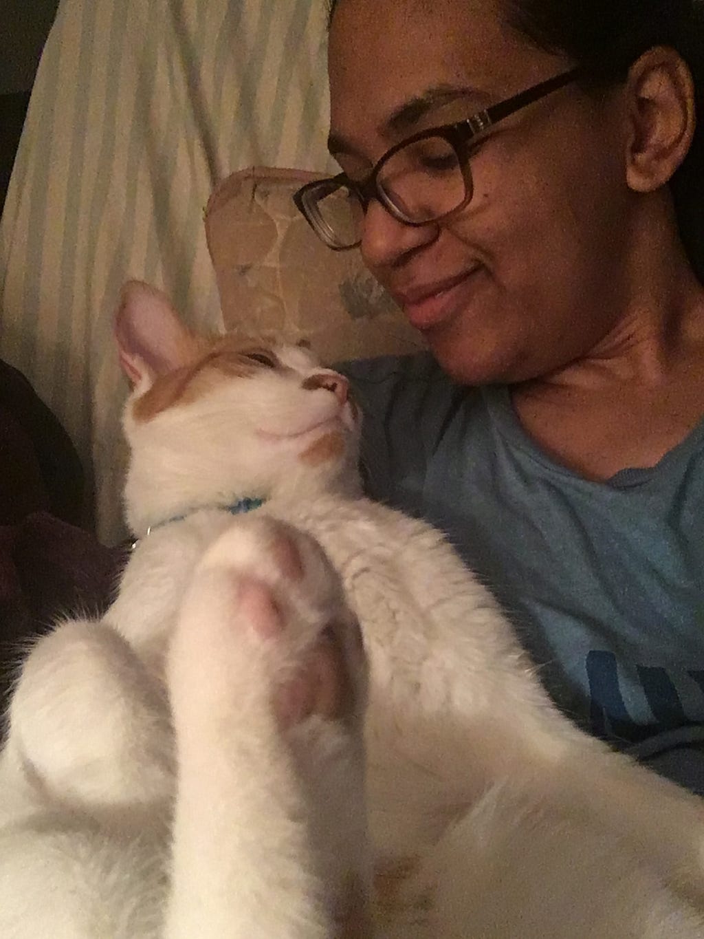 The author sitting down while holding the orange and white cat in the crook of her arm. The author and cat and are looking at each other.