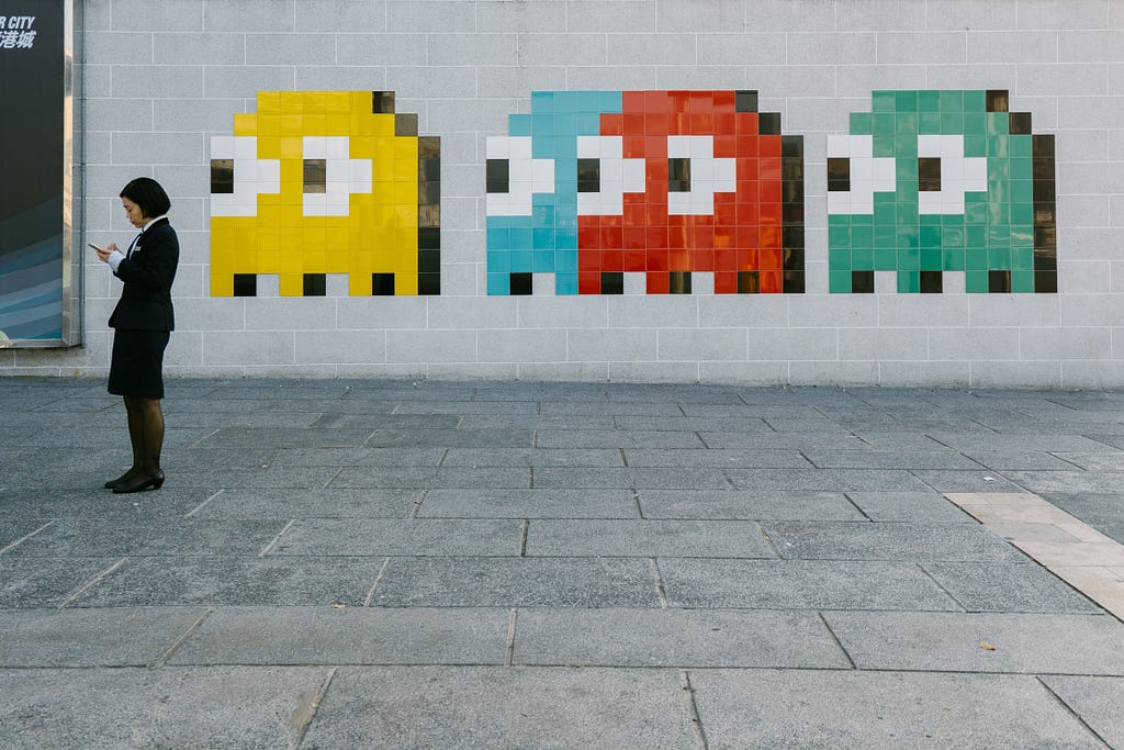 A person looks at their mobile phone while a row of PacMan ghosts look on from a mural behind them.