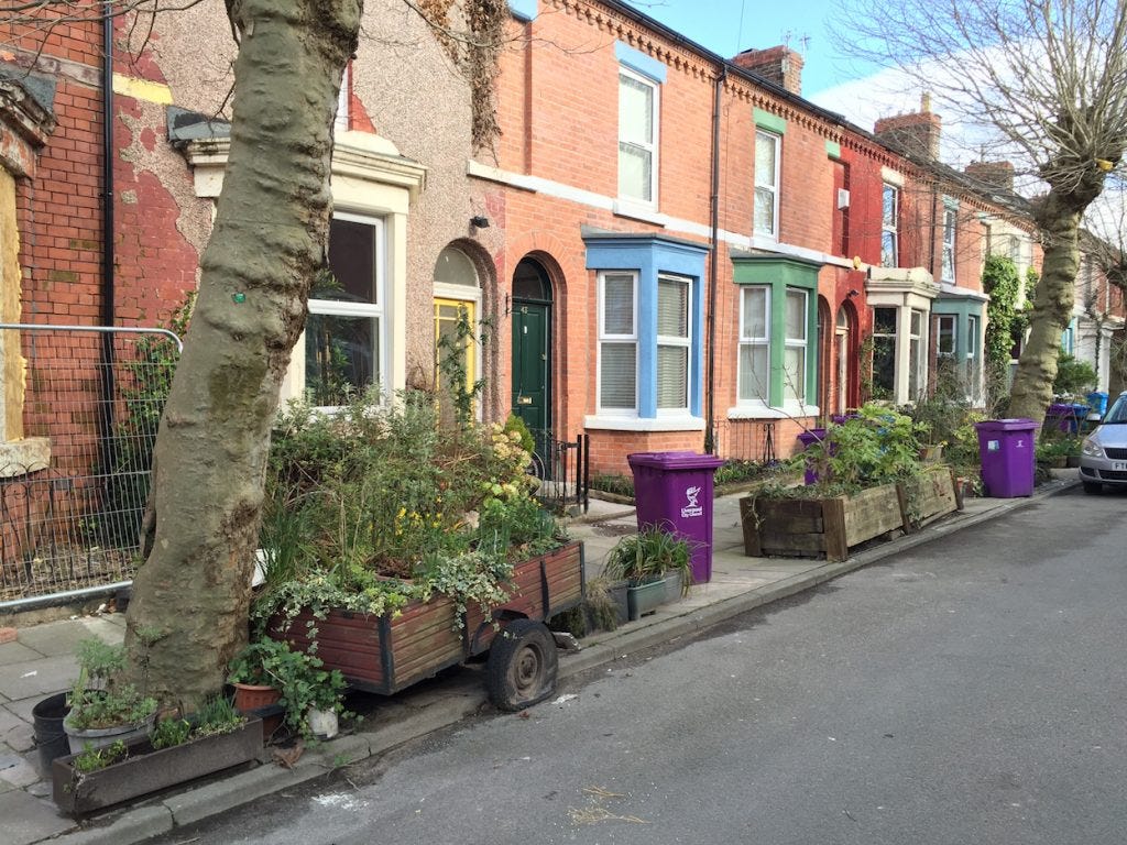 A street in Granby, Liverpool, with red-brick terraced houses decorated in bright colours and with flowers