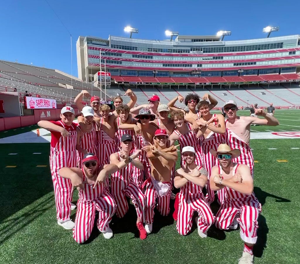 Tom and friends post for a photo in Memorial Stadium in matching red and white striped overalls