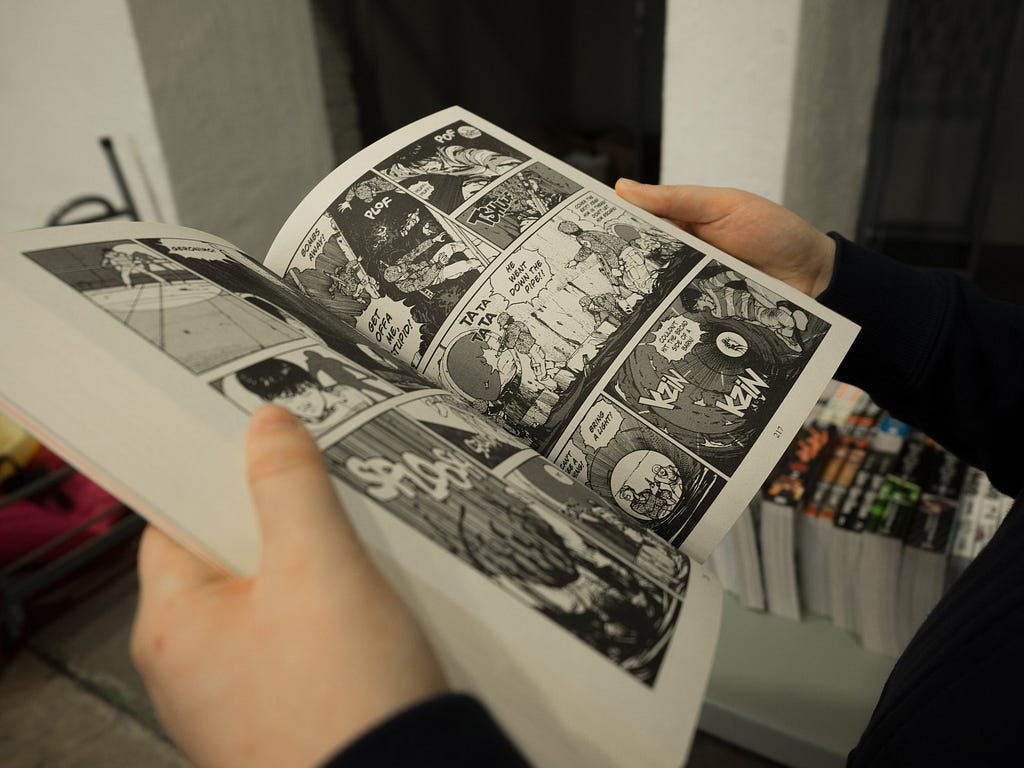 L’immagine mostra un libro di fumetti aperto e tenuto da una persona con entrambi le mani.