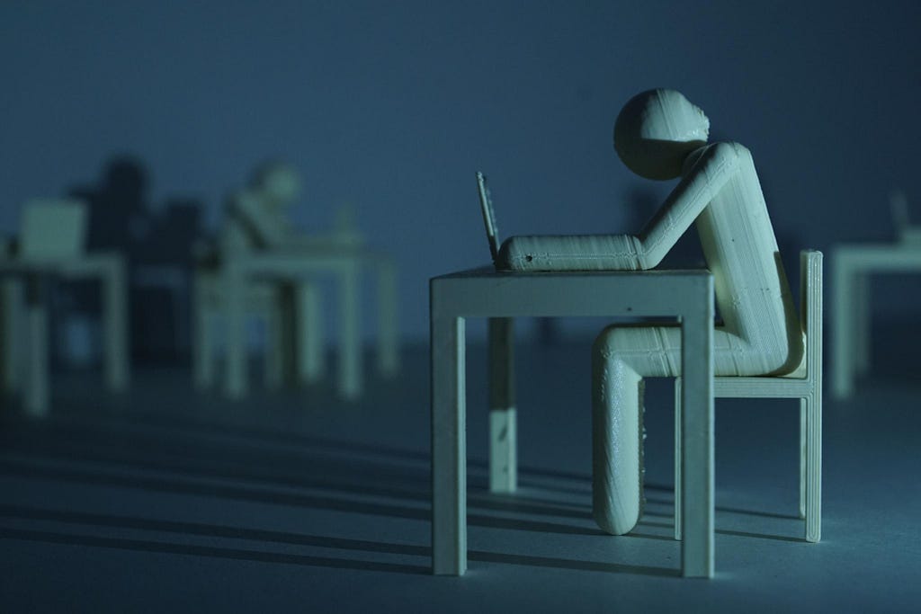 a wooden figure sitting at a desk looking at a laptop