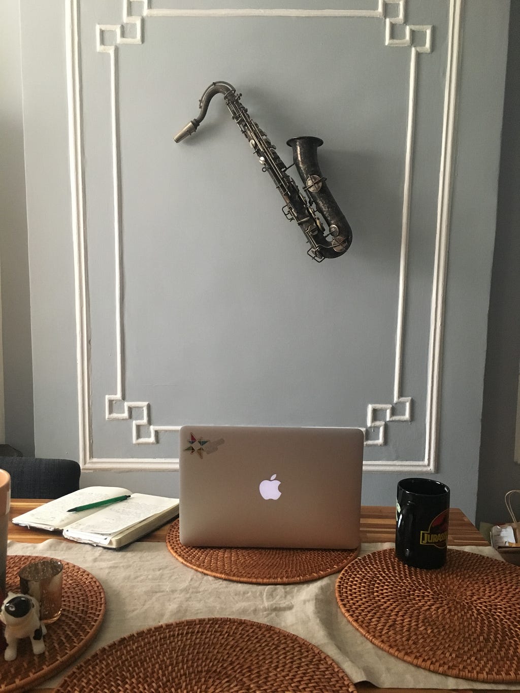 A saxophone hanging on a grey wall with a laptop open on a desk