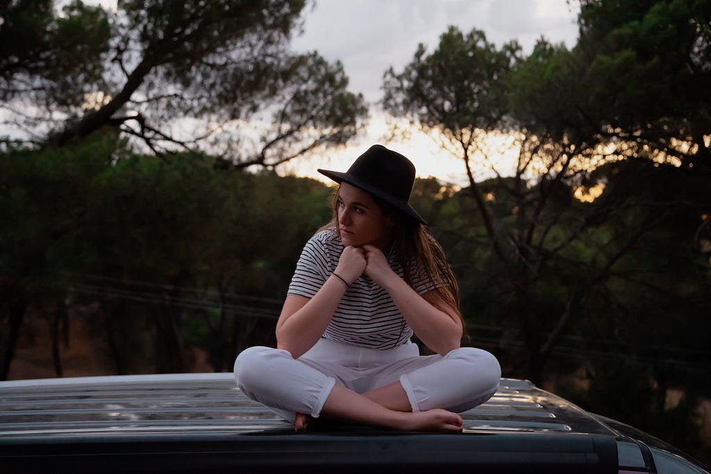 Lady wearing hat sat on roofdeck of Mercedes Sprinter camper looking thoughtful