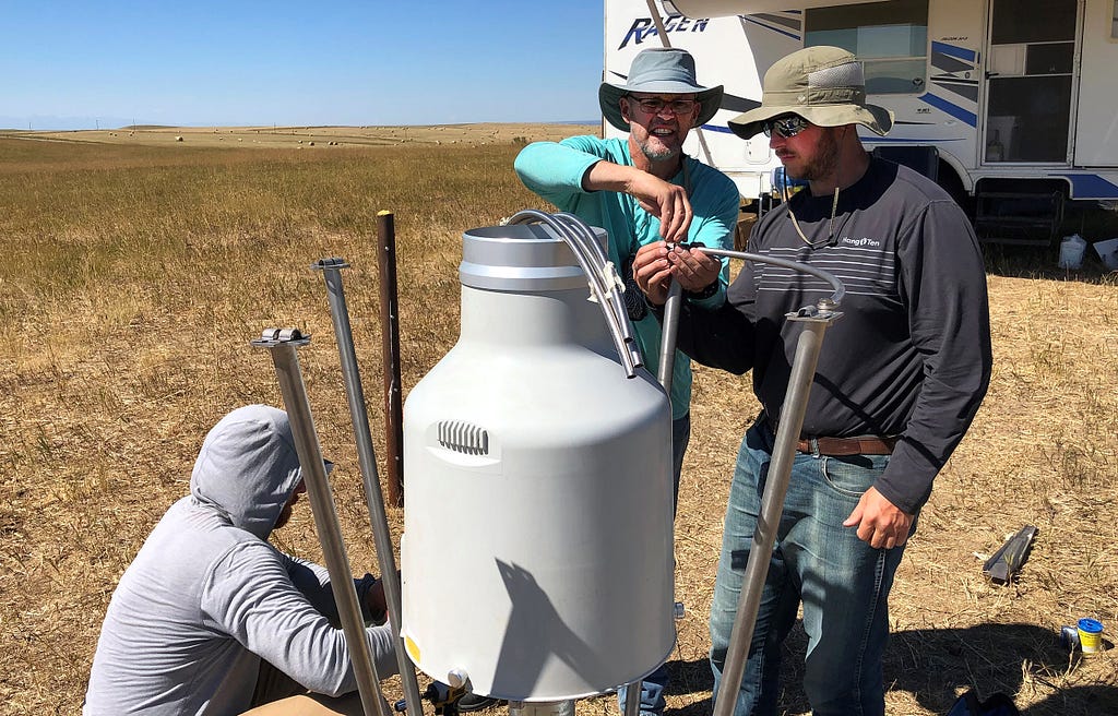 Three men install equipment on the Montana prairie near a camper.