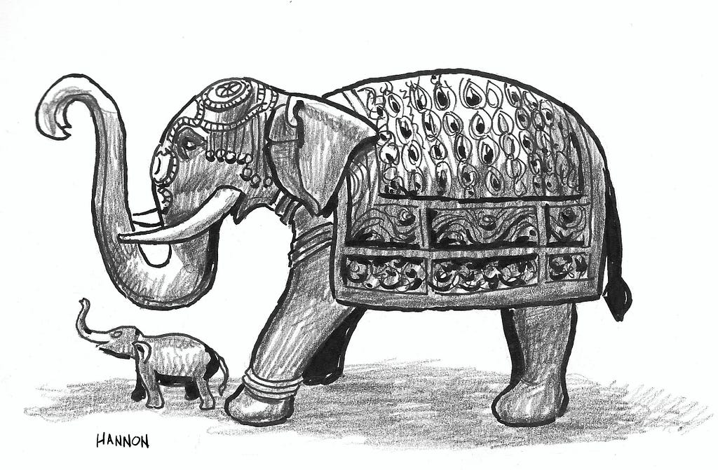 An elephant sculpture is shown with an ornate blanket on its back and an elaborate headdress. Its trunk is raised but curled down at its tip. A smaller, juvenile elephant is in front of the larger elephant, below its trunk.