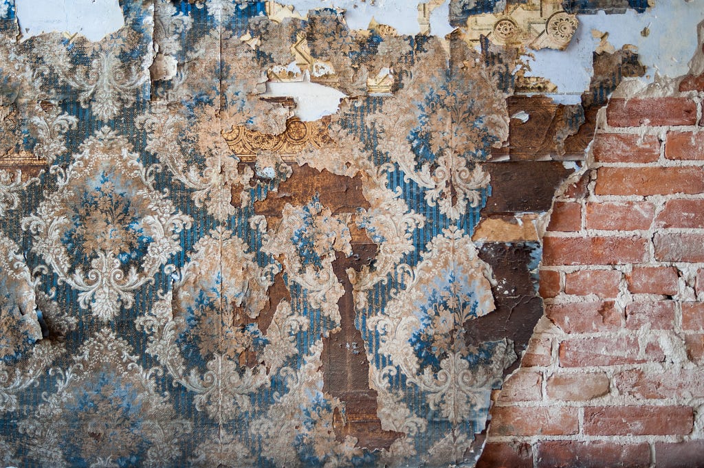 Image of old wallpaper, peeling paint and exposed brickwork