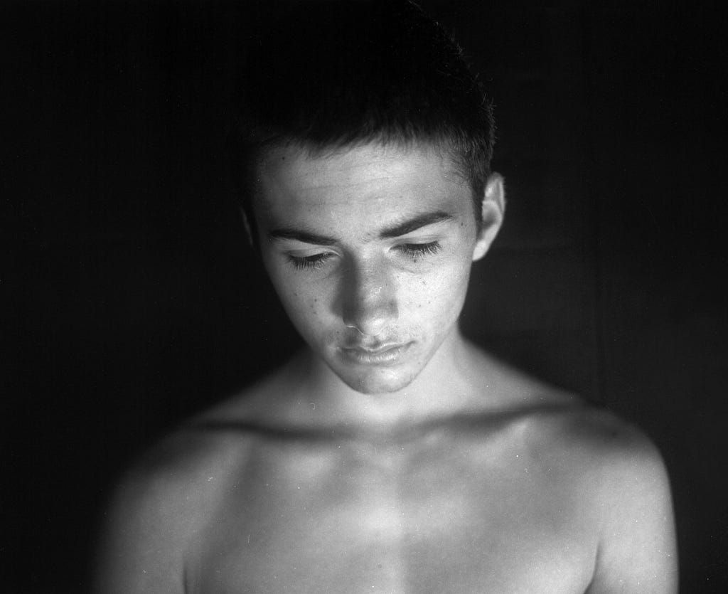shirtless young man with distant stare  looks down; tears on his face
