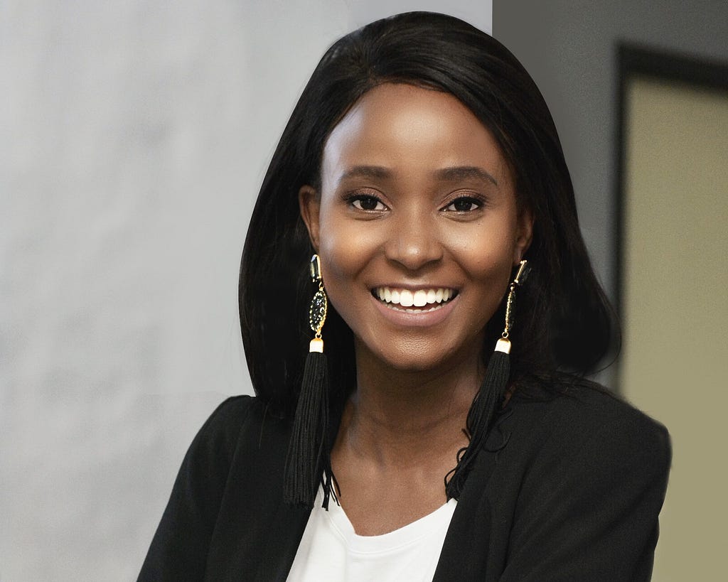 A young woman from Botswana smiles at the camera, with her arms folded. She wears a black blazer and white T-shirt.