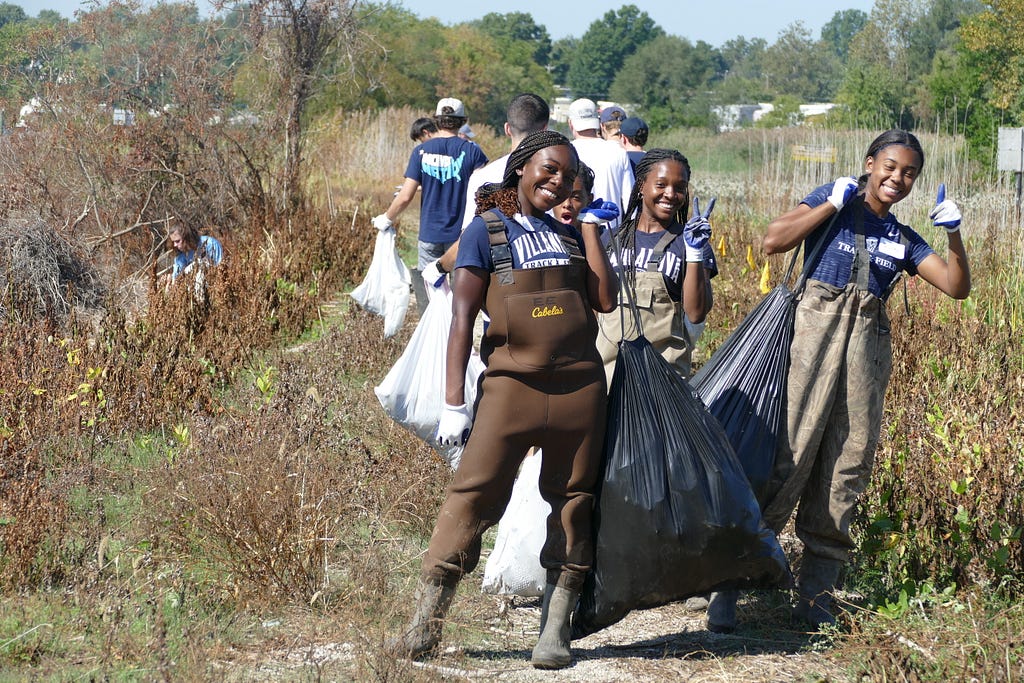 Four girls smile at camera wearing waders carrying full trash bags