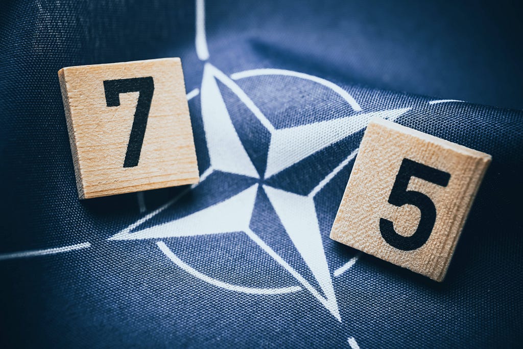 Wood blocks with the numbers 7 and 5 on top of fabric showing the NATO emblem. Photo by Christian Ohde/IMAGO/Reuters