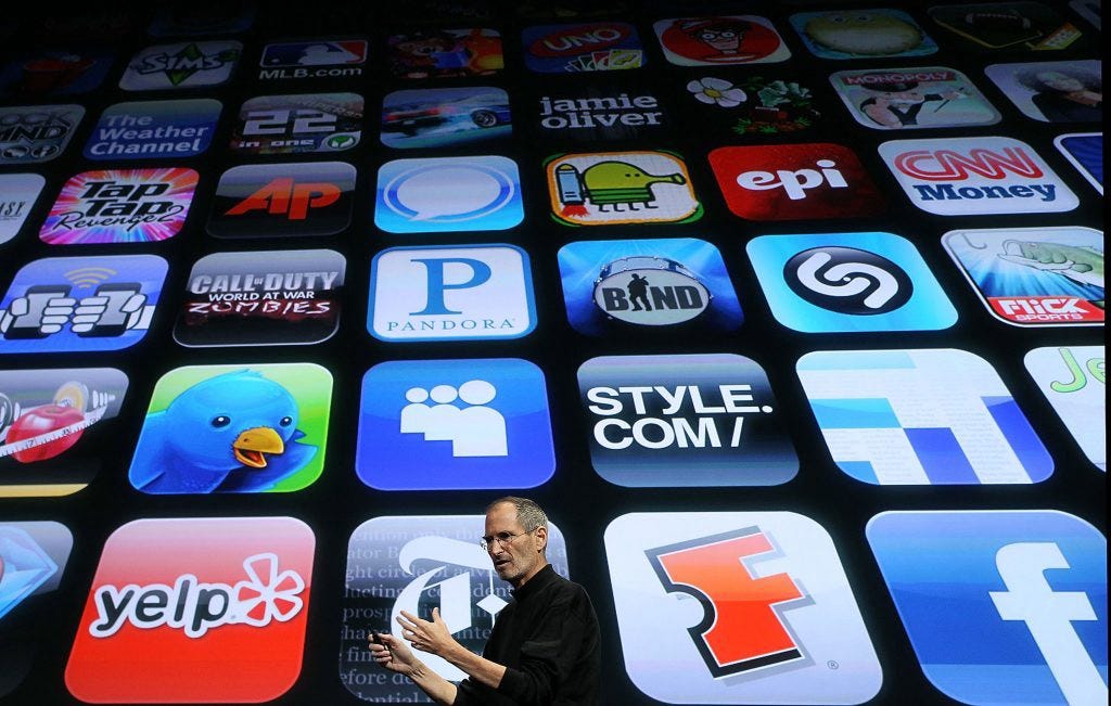 Steve jobs standing in front a giant screen displaying various mobile app icons
